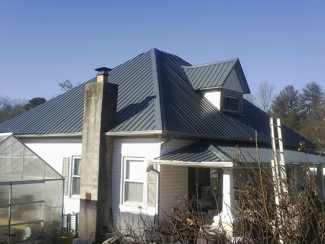 Dark blue standing seam metal roof on a white farmhouse with dormer — Slate & Tile Roof Repair by Roofing Brothers in Severn