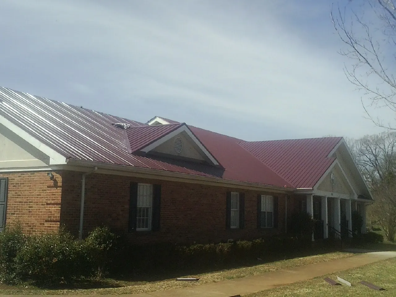 Red metal roof with gabled entries on a long brick building, from a Hail Damage Roof Repair job in Severn