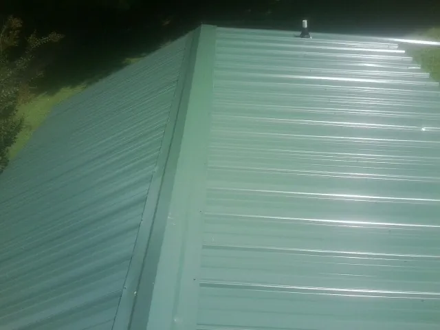 New green metal panels meeting at the ridge of a roof — Flat Roof Repair work by our crew in Severn
