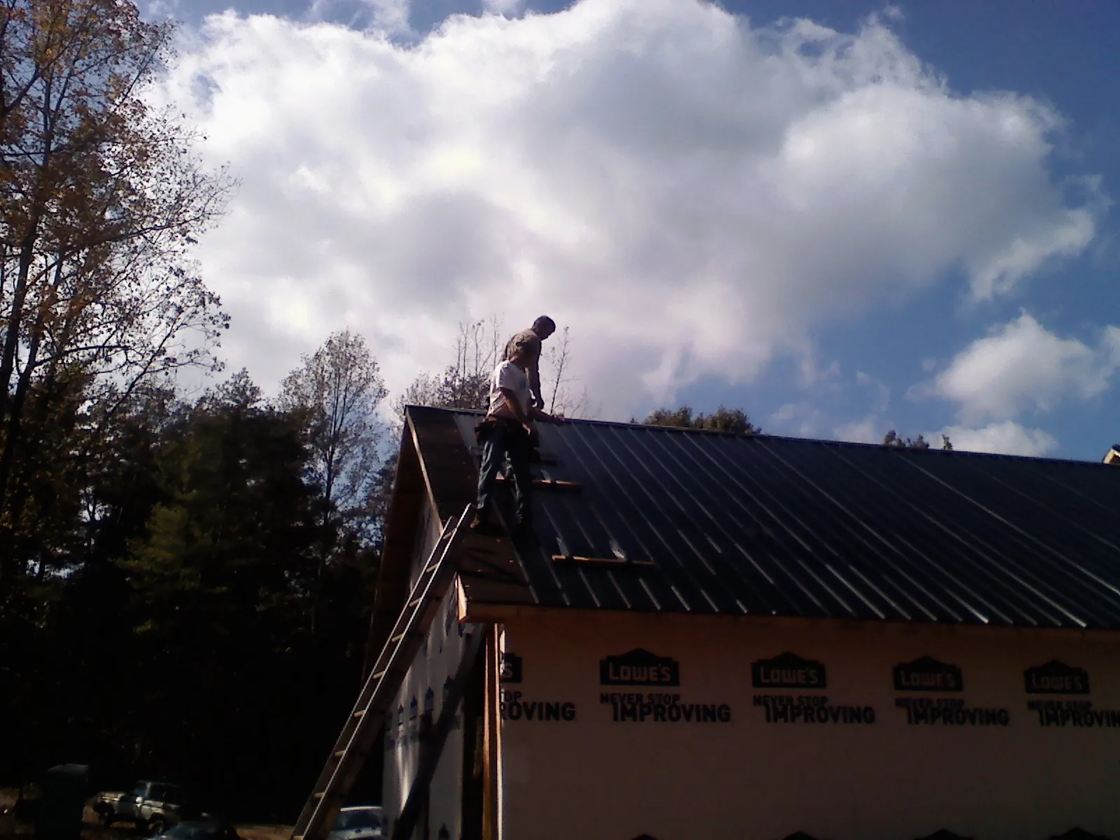 Roofer fastening dark metal panels high against a cloudy sky, from a Roof Inspection job in Severn