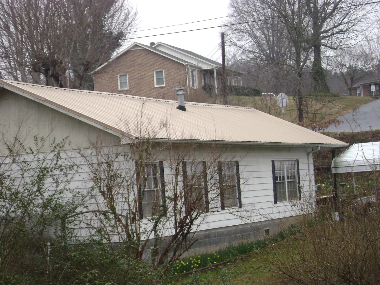 Tan metal roof on a white sided house set into a hillside — Commercial Roofing by Roofing Brothers in Severn